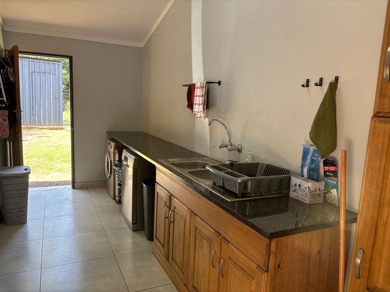Functional laundry room featuring built-in wooden cabinetry, granite countertops, a stainless steel sink, and direct access to the rear garden area.