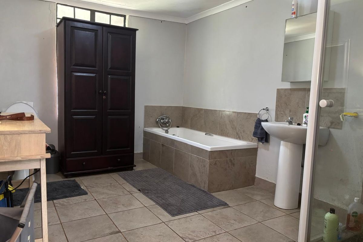 A functional bathroom featuring a tiled bathtub surround, pedestal washbasin, and neutral floor tiling, offering a practical layout with potential for cosmetic updates.