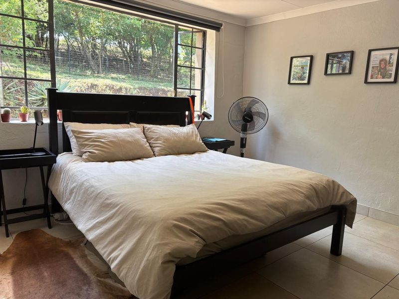 A bedroom featuring tiled flooring and a large window providing natural light and garden views.