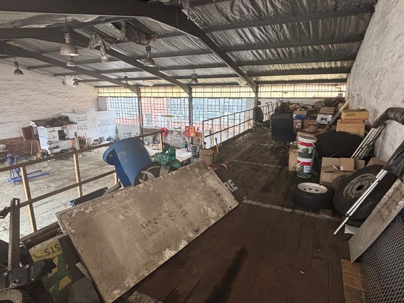 Industrial mezzanine level featuring exposed steel roof structure, industrial lighting, and large steel-framed windows, offering significant potential for workshop or storage use.