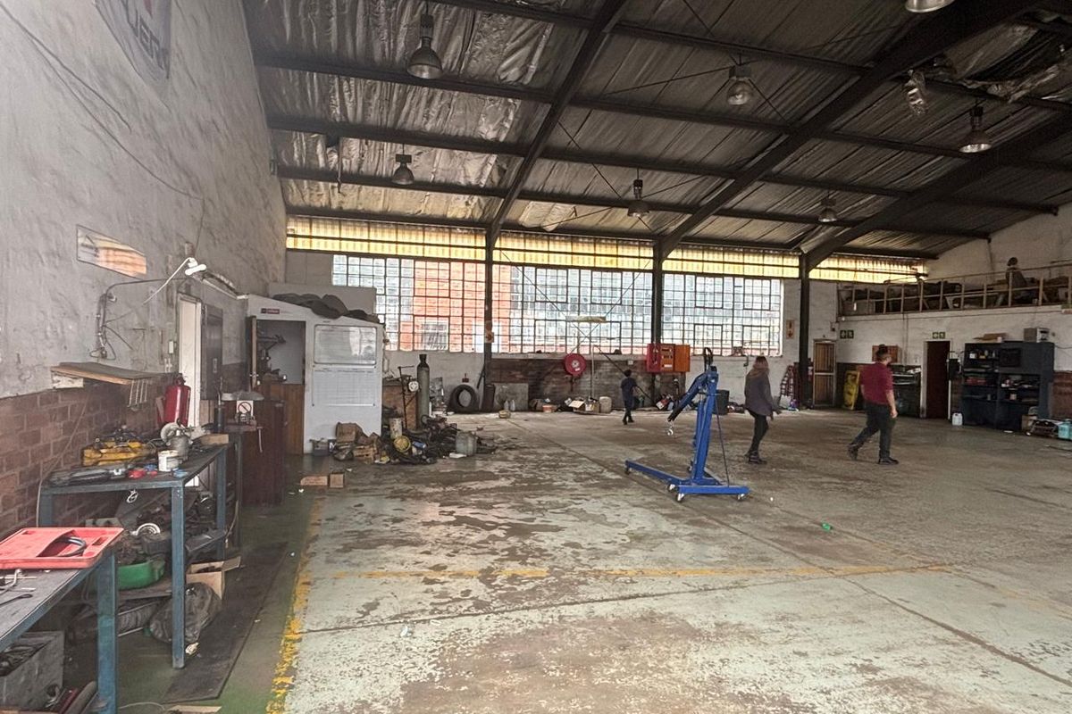 Spacious industrial utility area featuring high ceilings with exposed steel trusses, large metal-framed windows, and durable concrete flooring, suitable for workshop or storage use.