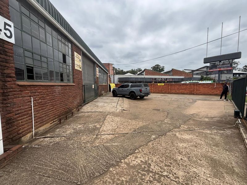 Industrial rear yard area featuring a brick facade, steel-framed windows, and a concrete surface enclosed by a brick boundary wall.