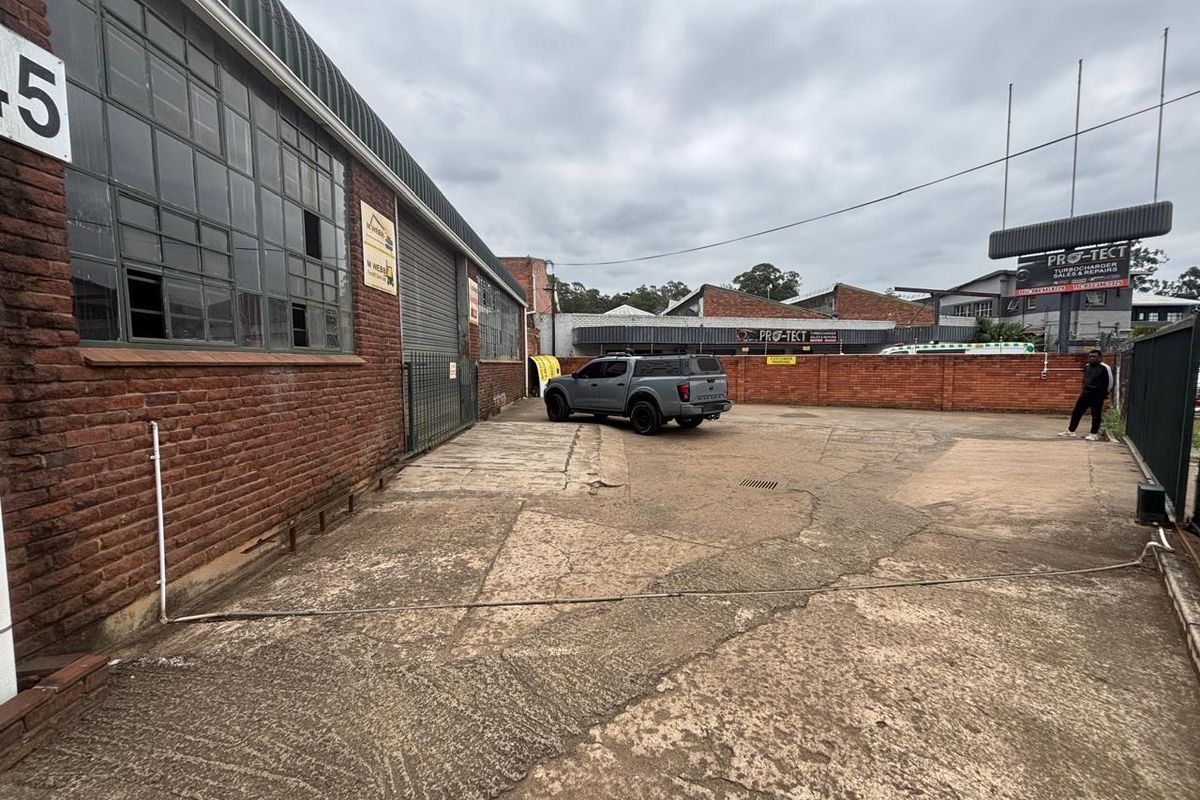 Industrial rear yard area featuring a brick facade, steel-framed windows, and a concrete surface enclosed by a brick boundary wall.