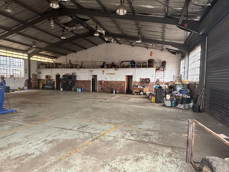Spacious industrial warehouse featuring a steel portal frame, mezzanine level, concrete flooring, and high-bay lighting, suitable for various commercial or manufacturing operations.
