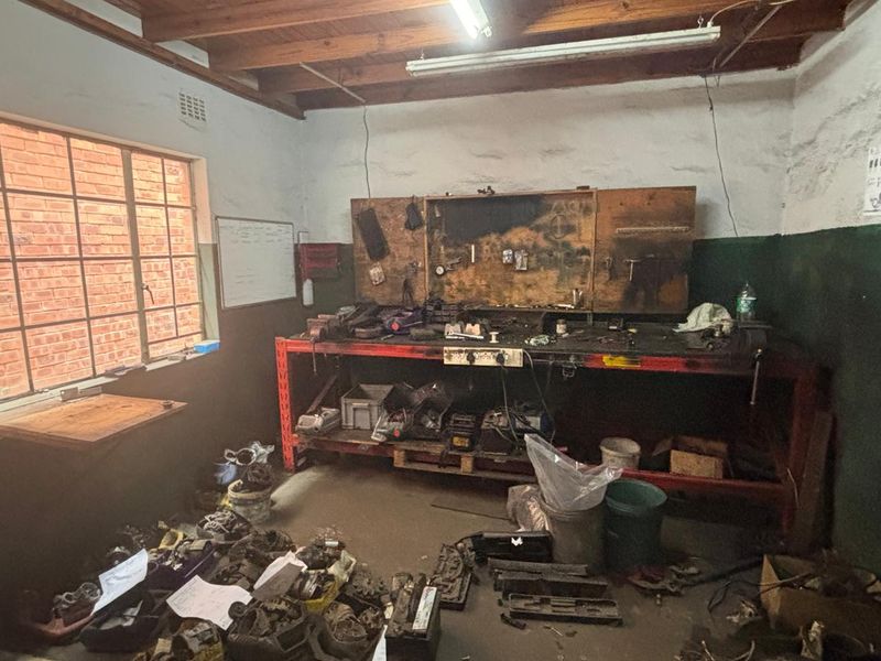 Industrial utility space featuring a built-in workbench, exposed timber ceiling beams, and a steel-framed window, suitable for workshop or storage use.