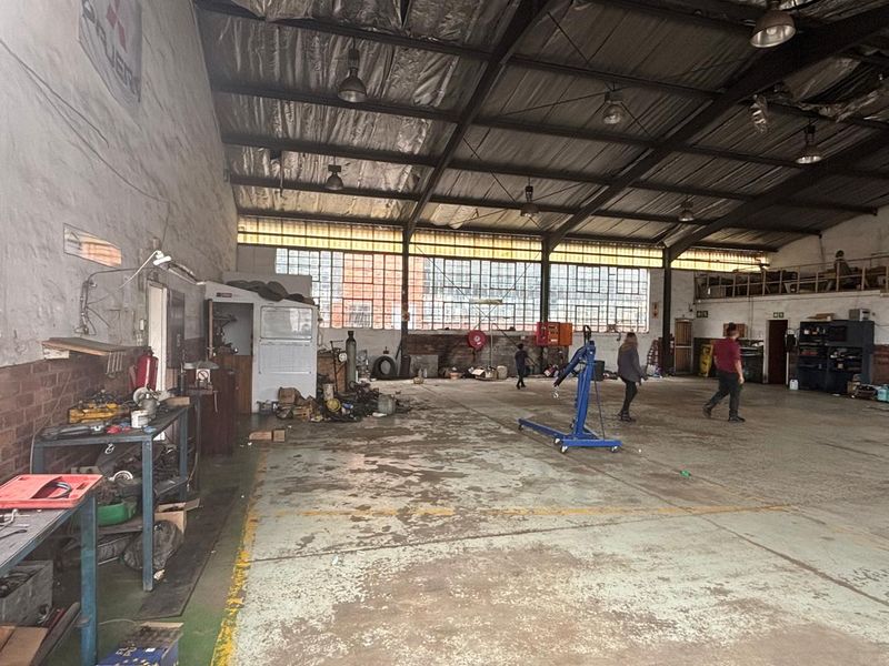 Spacious industrial utility area featuring high ceilings with exposed steel trusses, large metal-framed windows, and durable concrete flooring, suitable for workshop or storage use.