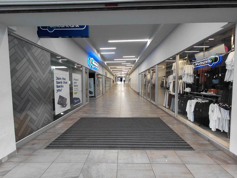 A well-maintained commercial shopping centre corridor featuring tiled flooring, recessed linear lighting, and glass-fronted retail storefronts.