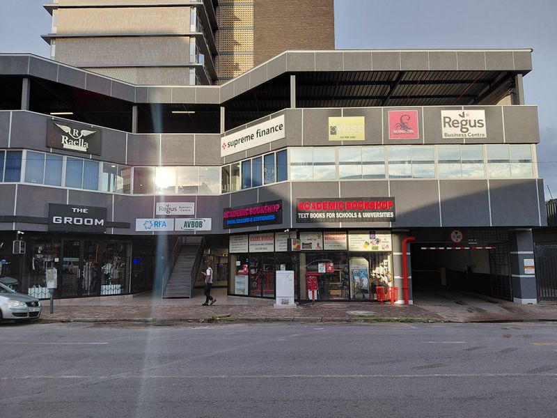 Street-level view of a multi-tenant commercial building featuring various retail storefronts, office signage, and a dedicated parking garage entrance.