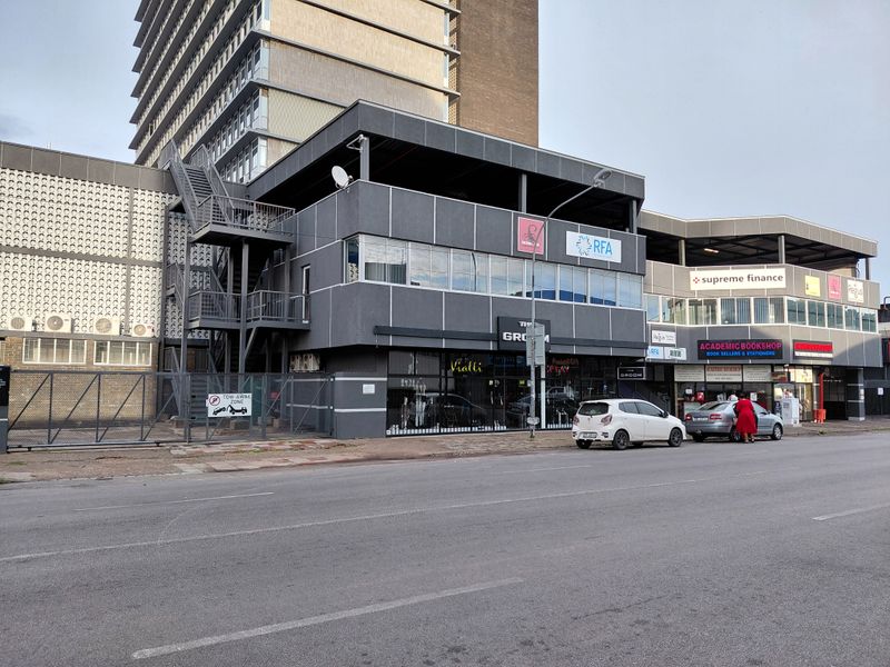 Street-level view of a multi-story commercial building featuring retail storefronts, office signage, and an external metal staircase.