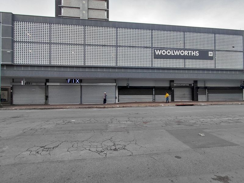 Commercial street-level retail frontage featuring multiple storefronts with security roller shutters and decorative metal cladding.
