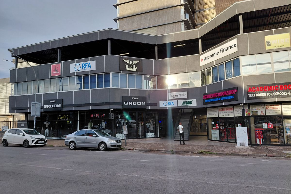 Street-level view of a multi-story commercial building featuring various retail storefronts, office signage, and a central pedestrian access staircase.