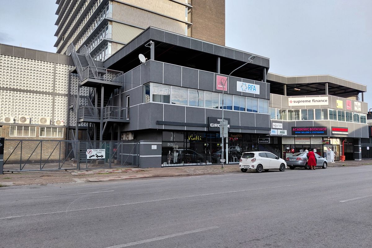 Street-level view of a multi-story commercial building featuring retail storefronts, office signage, and an external metal staircase.