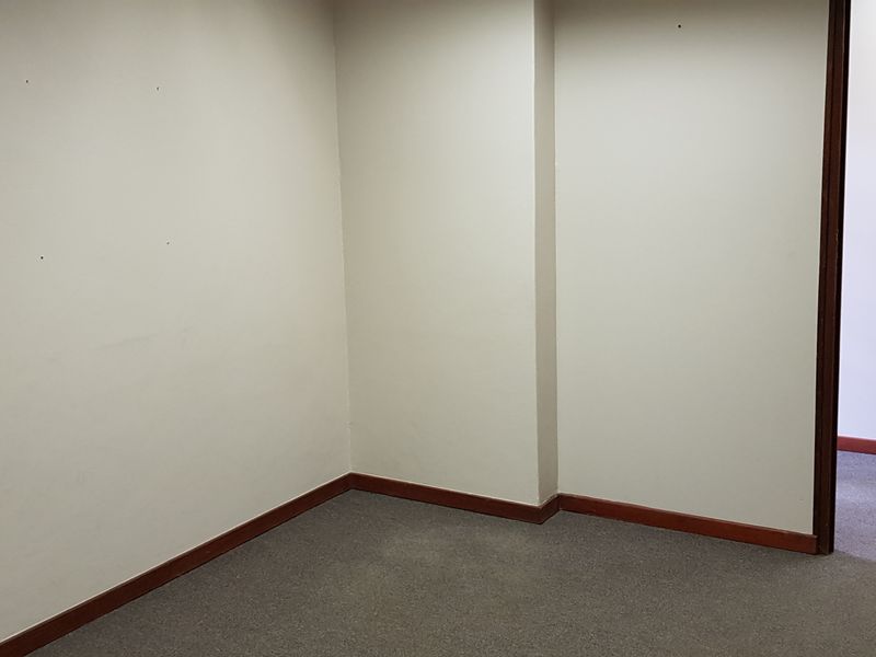 A vacant office space featuring neutral walls, carpet flooring, and a timber-framed door, providing a clean and functional environment for professional use.