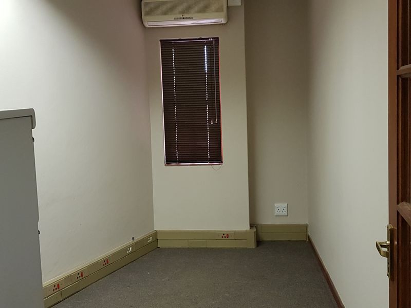 A functional, empty office space featuring carpeted flooring, wall-mounted air conditioning, and integrated electrical trunking along the baseboards.