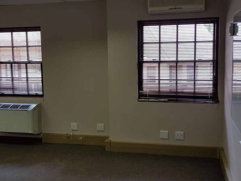 A vacant office space featuring neutral walls, carpeted flooring, built-in air conditioning, and a wall-mounted whiteboard, suitable for a professional work environment.