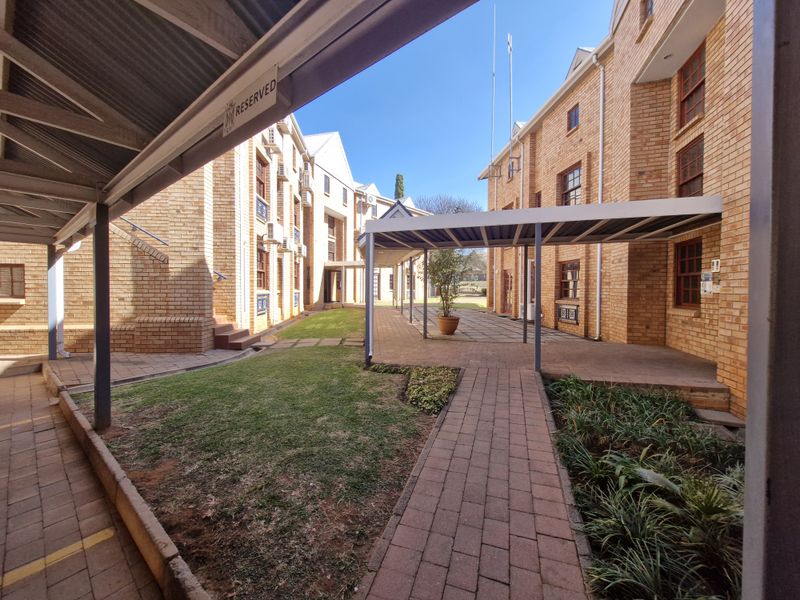 A well-maintained office complex courtyard featuring face brick buildings, covered walkways, paved paths, and landscaped garden areas.