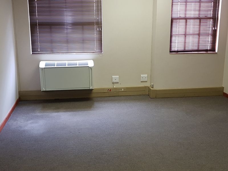 A vacant office space featuring carpet flooring, wall-mounted air conditioning, and venetian blinds on the windows.