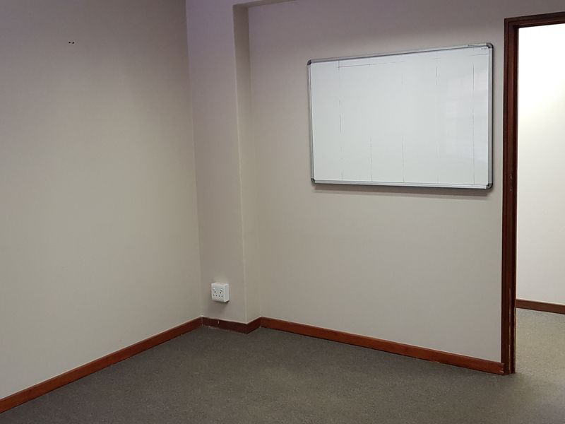 A vacant office space featuring neutral walls, carpeted flooring, a wall-mounted whiteboard, and a timber door leading to an adjacent room.