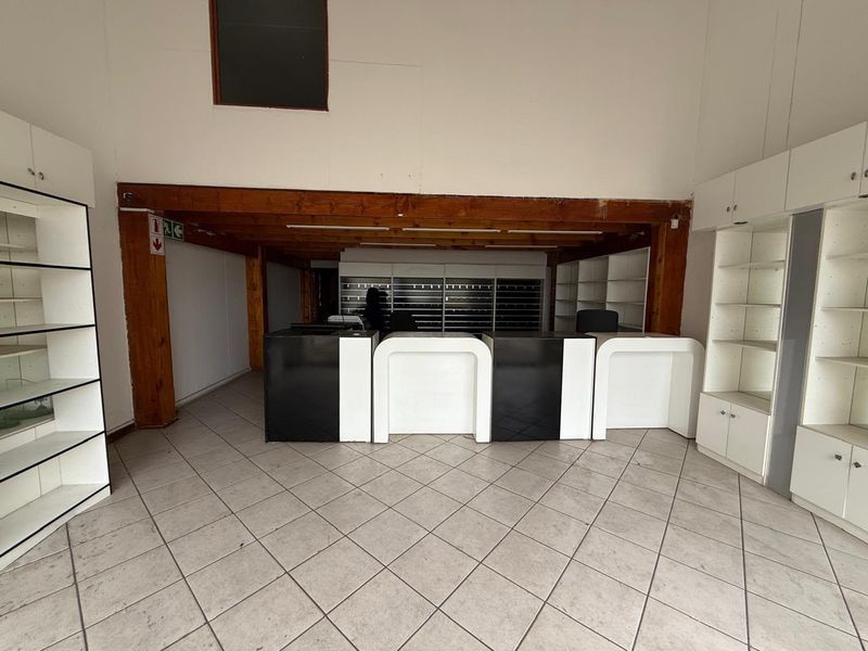 Industrial utility or retail space featuring tiled flooring, built-in shelving units, and a central reception counter under exposed timber ceiling beams.