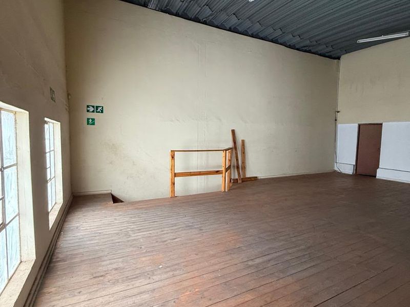 An open-plan industrial utility space featuring timber flooring, a corrugated metal ceiling, and large windows, suitable for storage or workshop use.