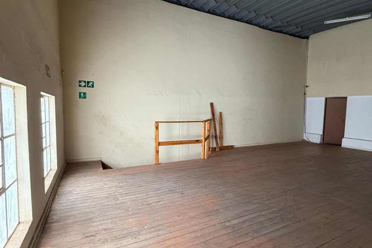 An open-plan industrial utility space featuring timber flooring, a corrugated metal ceiling, and large windows, suitable for storage or workshop use.