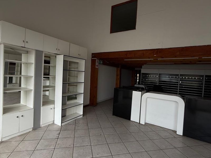 Open-plan industrial utility space featuring tiled flooring, built-in shelving units, and a timber mezzanine structure, suitable for retail or office use.