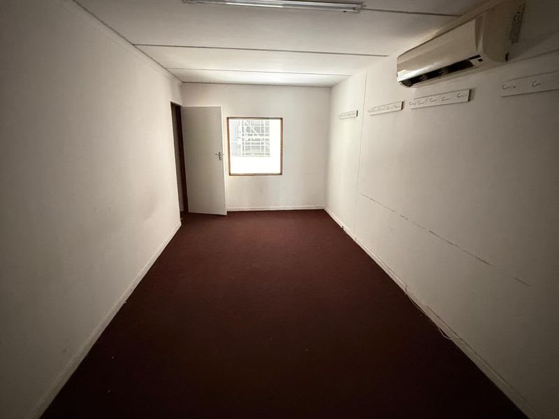 An empty, rectangular office space featuring carpeted flooring, wall-mounted air conditioning, and fluorescent lighting, suitable for a variety of commercial or industrial uses.