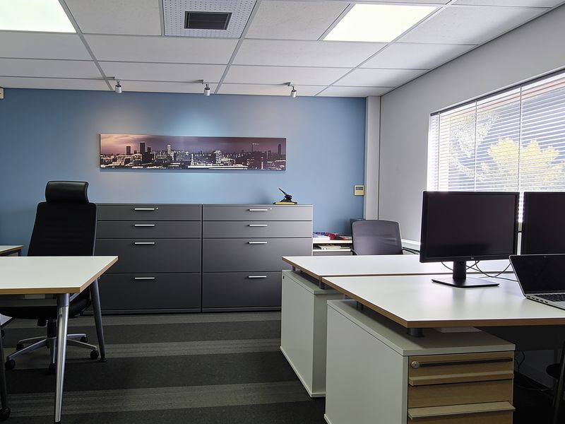 A professional office space featuring a suspended ceiling, recessed lighting, venetian blinds, and built-in storage cabinets with a modern blue accent wall.