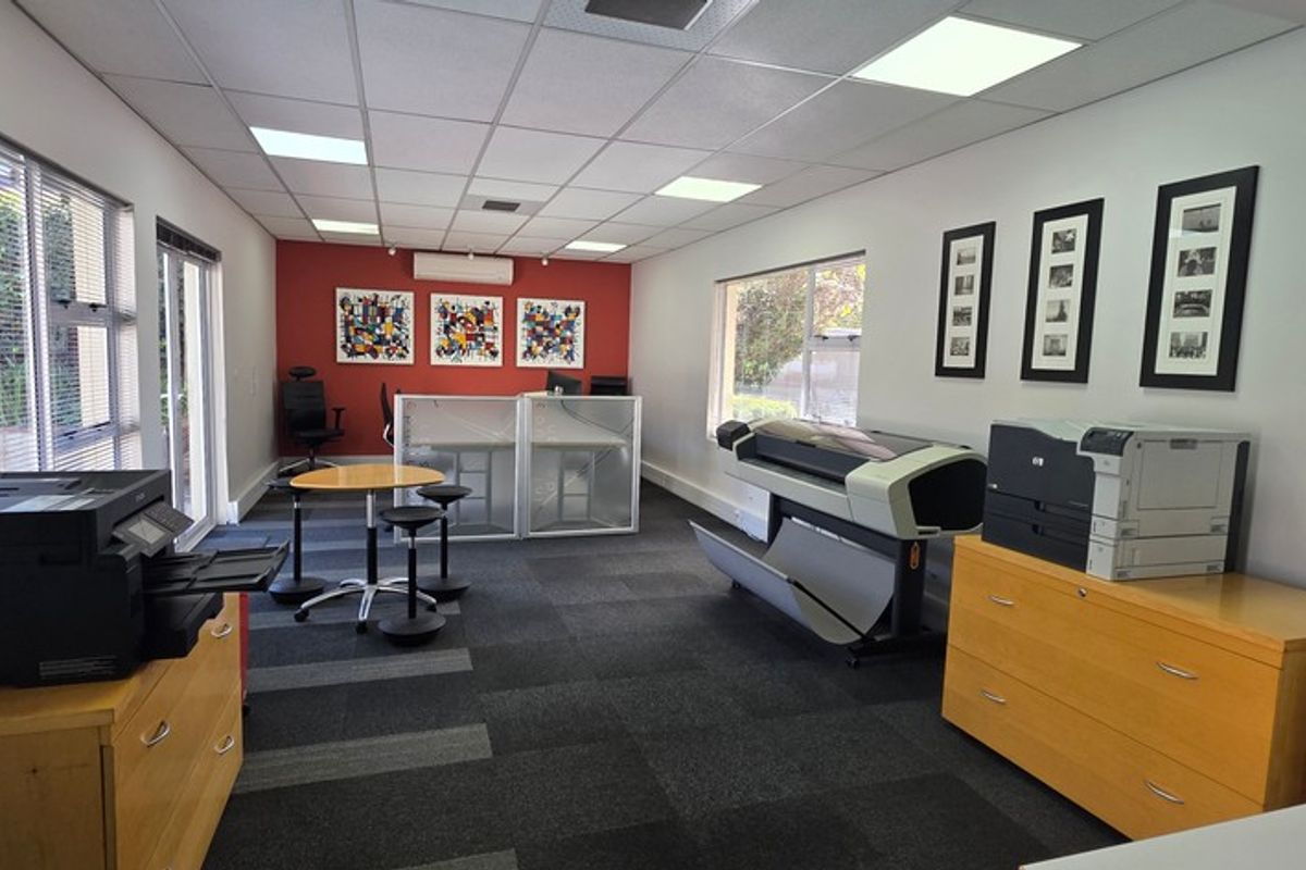A functional office space featuring carpeted flooring, a suspended ceiling with recessed lighting, and a wall-mounted air conditioning unit.