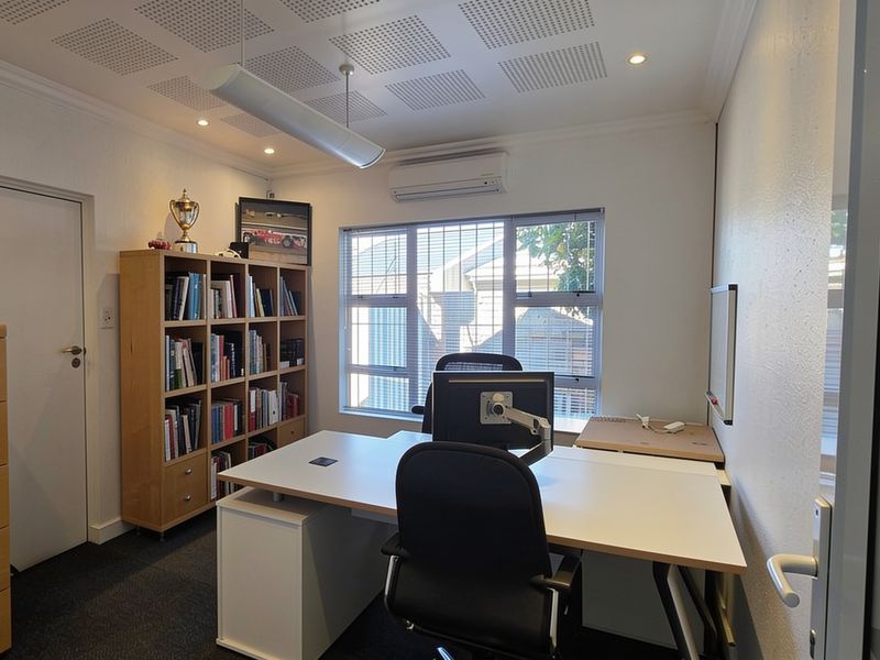 A well-maintained office space featuring acoustic ceiling tiles, split-system air conditioning, and large windows providing natural light.