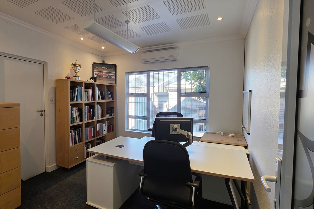 A well-maintained office space featuring acoustic ceiling tiles, split-system air conditioning, and large windows providing natural light.