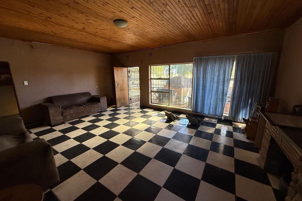 Spacious living area featuring a timber ceiling, checkered tile flooring, and a brick fireplace, offering a dated but functional industrial-style space.