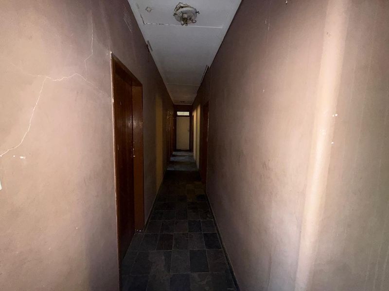 A narrow interior hallway featuring dark tiled flooring and multiple doorways, currently showing signs of wear and requiring cosmetic updates.
