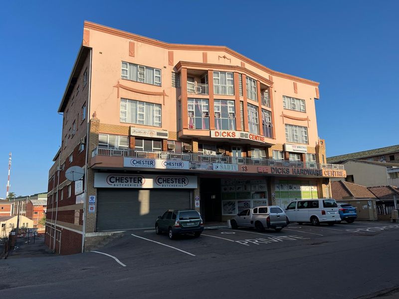 Front elevation of a multi-story commercial building featuring ground-level retail space with roller shutter doors, upper-level offices, and dedicated paved parking.