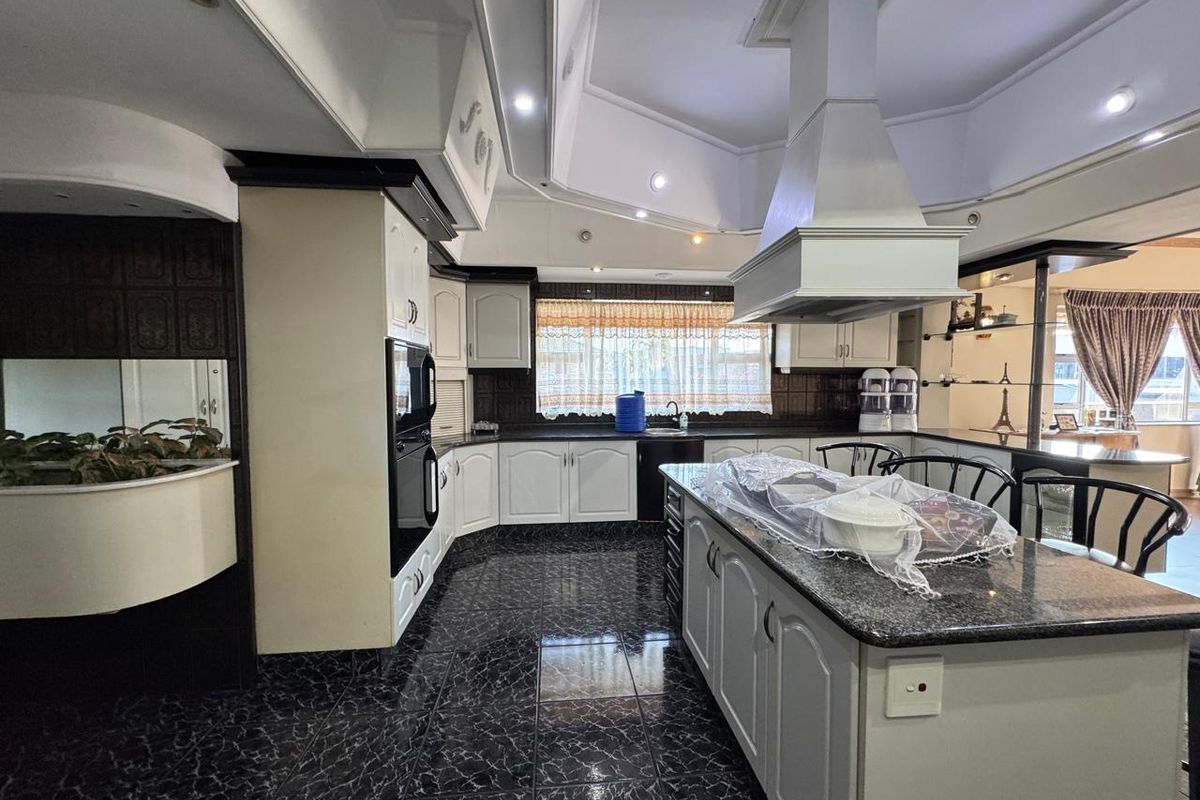 Spacious kitchen featuring a large central island, granite countertops, built-in oven, extractor fan, and extensive cabinetry with a modern tiled floor finish.