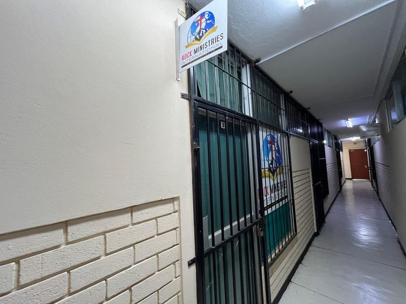 A commercial hallway featuring a security gate entrance with signage, tiled flooring, and overhead fluorescent lighting.