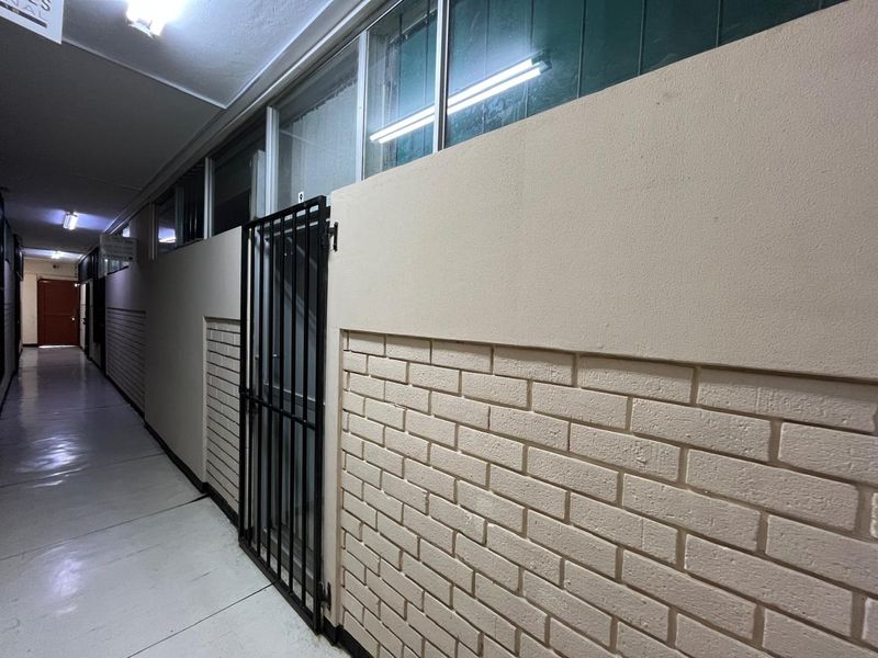 A commercial hallway featuring painted brickwork, security gates, and overhead fluorescent lighting, providing access to individual office or utility units.