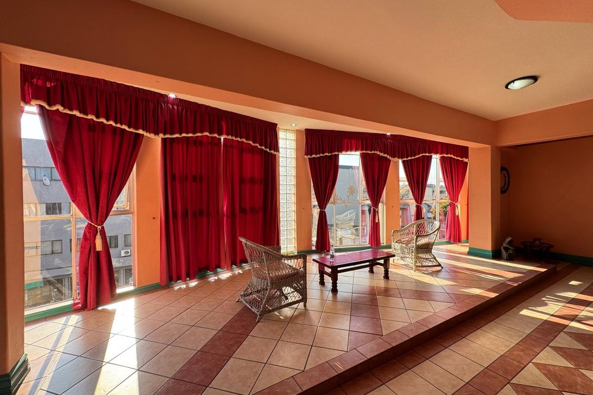 Spacious living area featuring a raised platform, decorative tiled flooring, and large windows with red curtains, offering a bright and open commercial space.