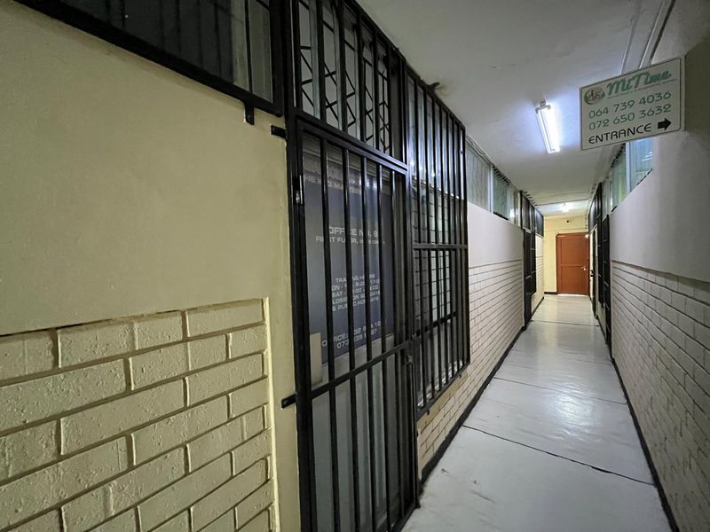 A commercial hallway featuring tiled flooring, brick walls, and security gates leading to office entrances.