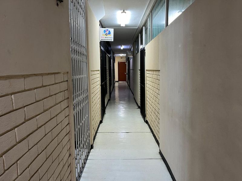 A commercial hallway featuring tiled flooring, brickwork wall accents, and security gates leading to various office or unit entrances.