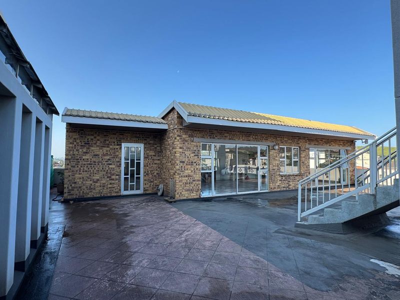 Rear exterior view of a commercial building featuring a face brick facade, sliding glass doors, and an expansive tiled patio area with external staircase access.