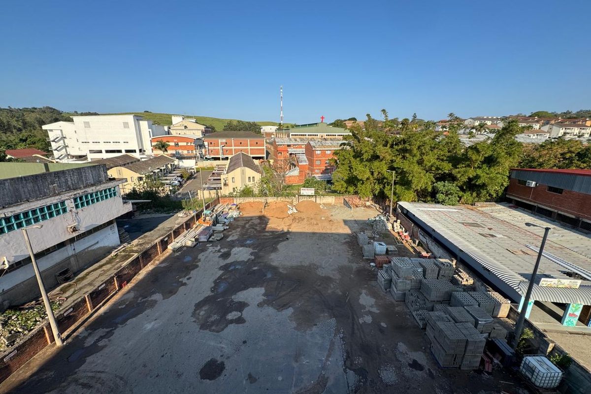 Aerial view of a commercial property yard featuring paved surfaces, boundary walls, and surrounding industrial and residential buildings.