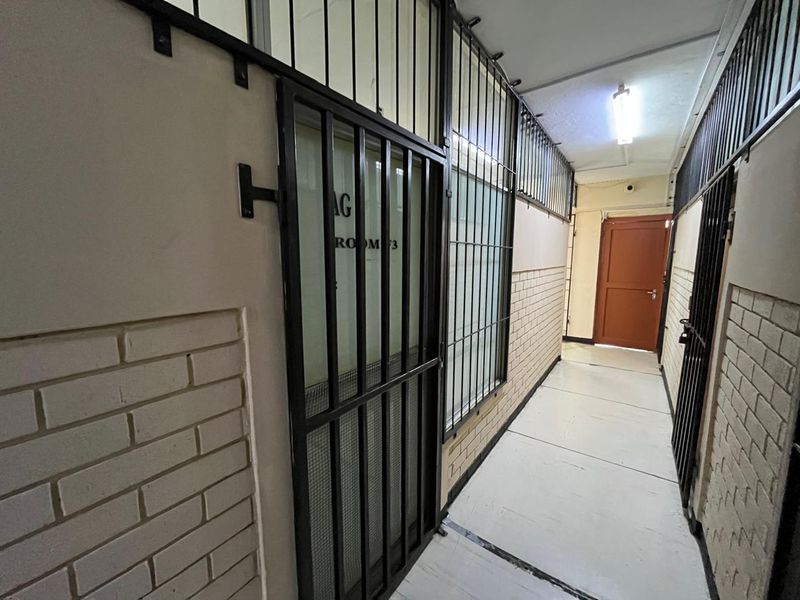 A commercial hallway featuring security gates, brick wall detailing, and fluorescent lighting, providing access to office or utility spaces.