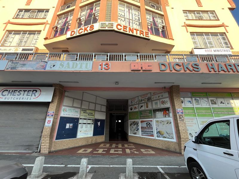 Front elevation of Dicks Centre, a commercial building featuring ground-floor retail units with roller shutter doors and upper-level office or residential windows.