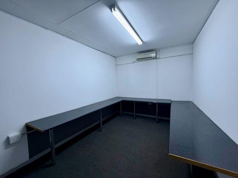 A functional, empty office space featuring built-in wrap-around desks, carpeted flooring, and a wall-mounted air conditioning unit.