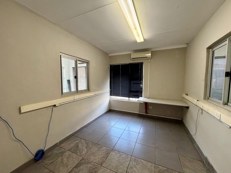 A functional, empty office space featuring tiled flooring, built-in desk, split-system air conditioning, and integrated electrical trunking along the walls.