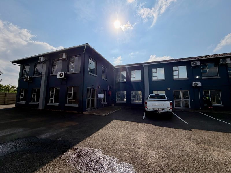 Exterior view of a multi-story commercial building featuring dark blue facade, aluminum windows, and dedicated asphalt parking area with wall-mounted air conditioning units.