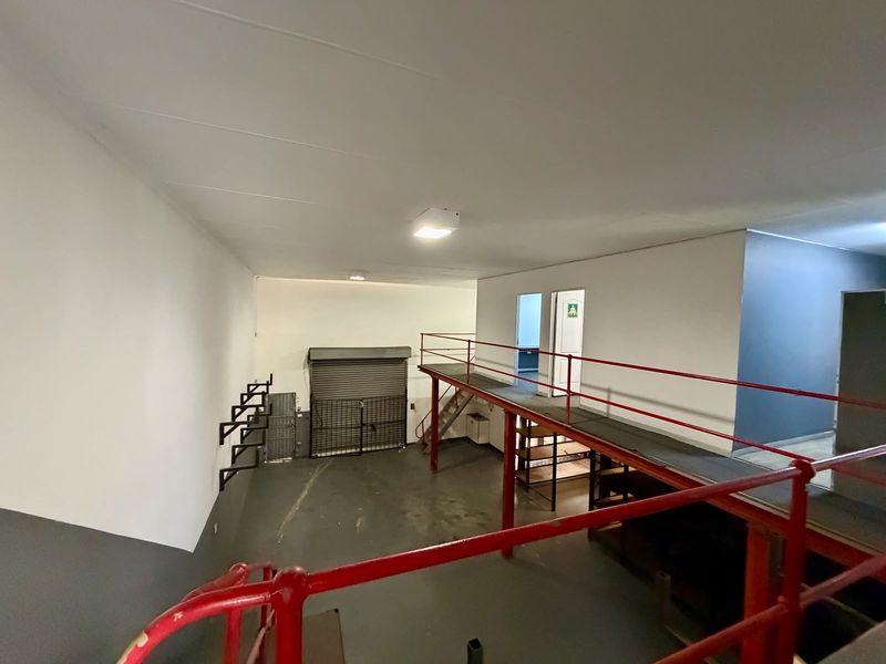 Spacious commercial utility area featuring a mezzanine level with metal safety railings, industrial flooring, and a secure roller shutter door access.