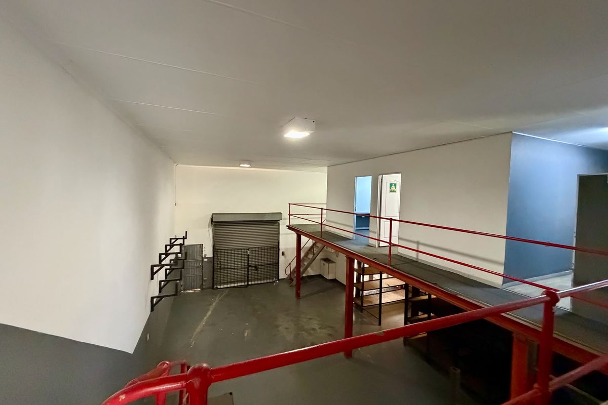 Spacious commercial utility area featuring a mezzanine level with metal safety railings, industrial flooring, and a secure roller shutter door access.