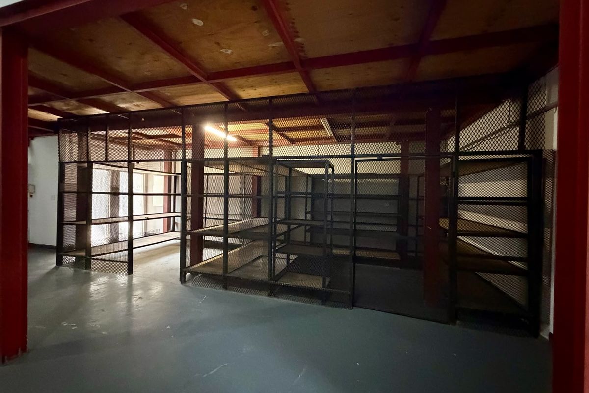 A functional utility or storage area featuring industrial-style metal mesh partitioning, exposed steel ceiling beams, and durable epoxy-coated flooring.